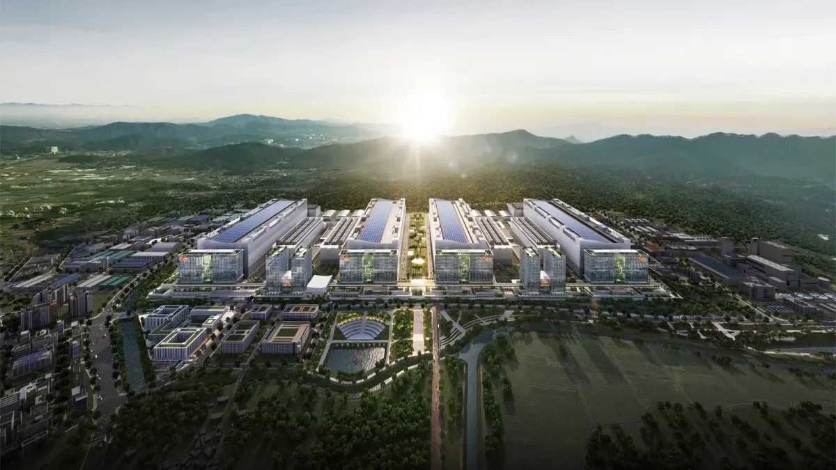 Aerial view of a modern industrial complex with large white buildings, green landscaping, and mountains in the background at sunrise.