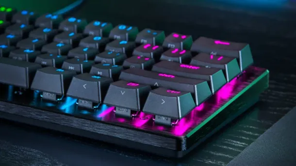 Compact black keyboard with vibrant RGB backlighting, angled keys, and a sleek carbon-fiber textured base.