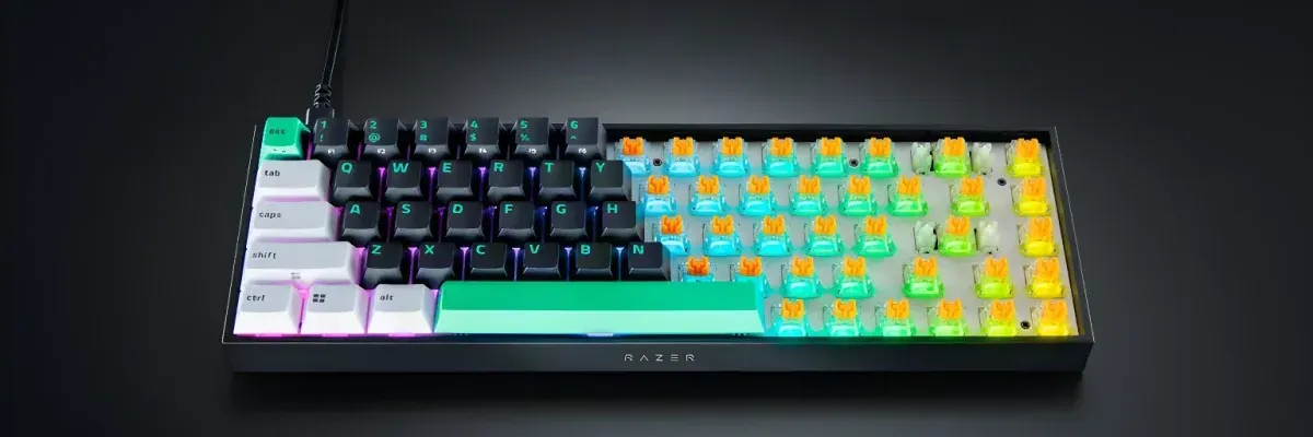 Compact black mechanical keyboard with vibrant RGB lighting, exposed switch stems, and a wired connection on a dark surface.